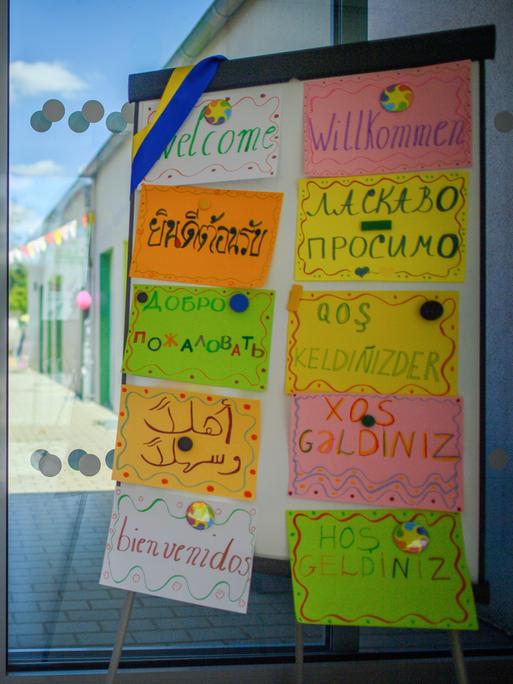 Eine Tafel mit Schildern, auf denen in zehn unterschiedlichen Sprachen "Willkommen" zu lesen ist, steht im Eingangsbereich einer Kita