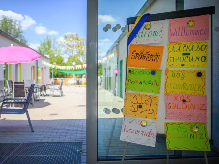 Eine Tafel mit Schildern, auf denen in zehn unterschiedlichen Sprachen "Willkommen" zu lesen ist, steht im Eingangsbereich einer Kita