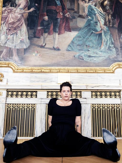 Liv Strömquist sitzt breitbeinig in schwarzen Klamotten auf dem Boden.