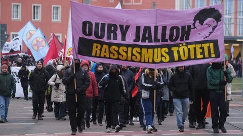 Teilnehmer einer linken Demonstration gehen mit Transparenten und Fahnen durch die Stadt. Auf einem Transparent steht "Oury Jalloh - Rassismus tötet" 