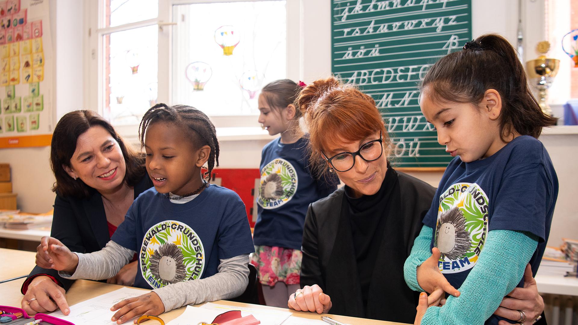 Drei Kinder mit T-Shirts der Spreewaldschule sitzen mit zwei Erwachsenen an einem Tisch in einem Klassenraum. Drei Kinder mit T-Shirts der Spreewaldschule sitzen mit zwei Erwachsenen an einem Tisch in einem Klassenraum.