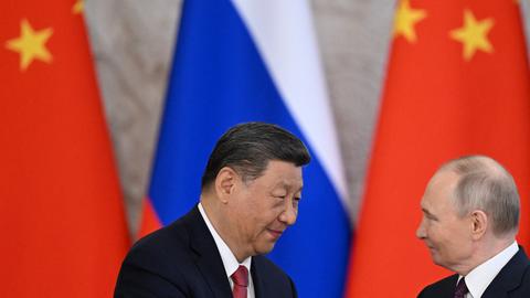Xi Jinping (links) und Wladimir Putin (rechts im Bild) stehen vor der russischen und der chinesischen Flagge und schütteln sich die Hände.