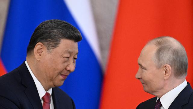 Wladimir Putin und Xi Jinping stehen vor der russischen und der chinesischen Flagge und schütteln sich die Hände.