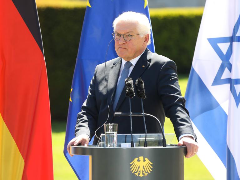 Bundespräsident Frank Walter Steinmeier bei der Pressekonferenz im Schloss Bellevue in Berlin. Er steht an einem Redepult. Hinter ihm sind die deutsche, die israelische und die EU-Flagge zu sehen. 