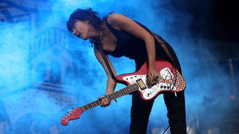 Courtney Barnett steht locker, vorn übergebeugt mit ihrer roten Gitarre auf einer blau erleuchteten Bühne.