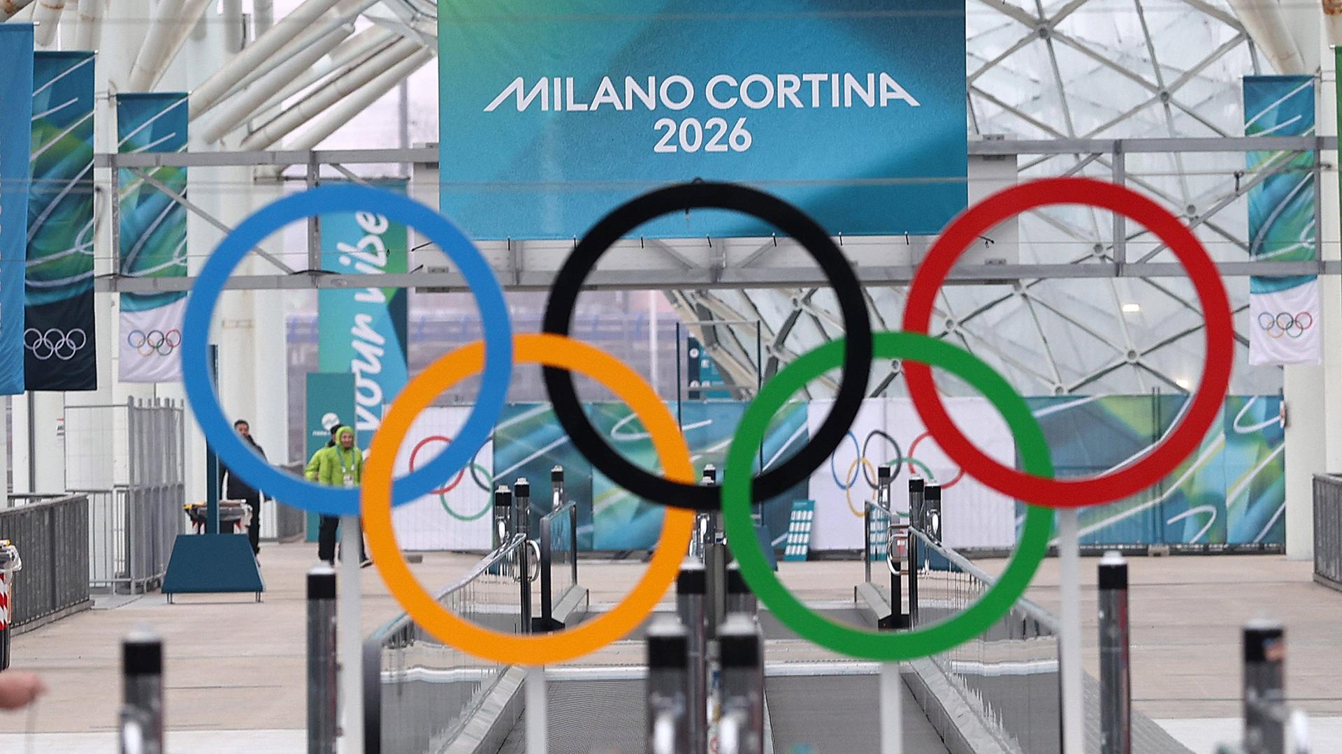 Die olympischen Ringe hängen vor einem Plakat mit der Aufschrift "Milano Cortina 2026".