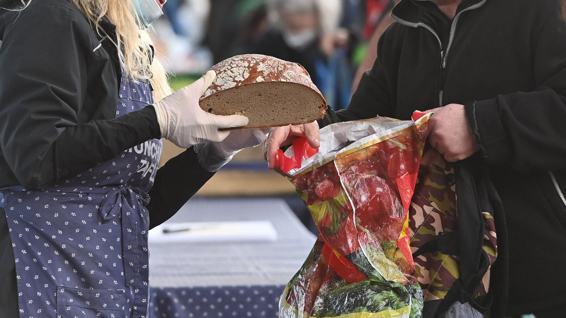 Bedürftige Menschen bei einer Tafel bei der Ausgabe von Lebensmitteln, ein Brot wird in eine Plastiktüte gesteckt.