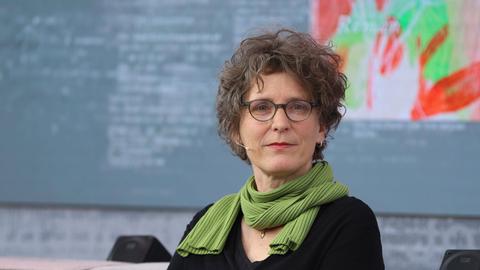 Die Autorin Annette Pehnt sitzt mit schwarzem Pullover und Schal auf einem Sofa und schaut in die Kamera