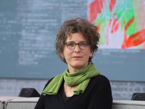 Die Autorin Annette Pehnt sitzt mit schwarzem Pullover und Schal auf einem Sofa und schaut in die Kamera