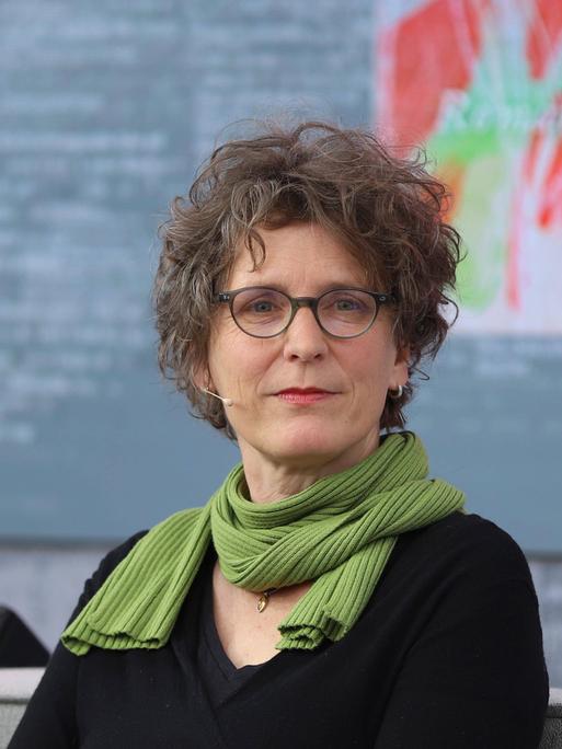 Die Autorin Annette Pehnt sitzt mit schwarzem Pullover und Schal auf einem Sofa und schaut in die Kamera