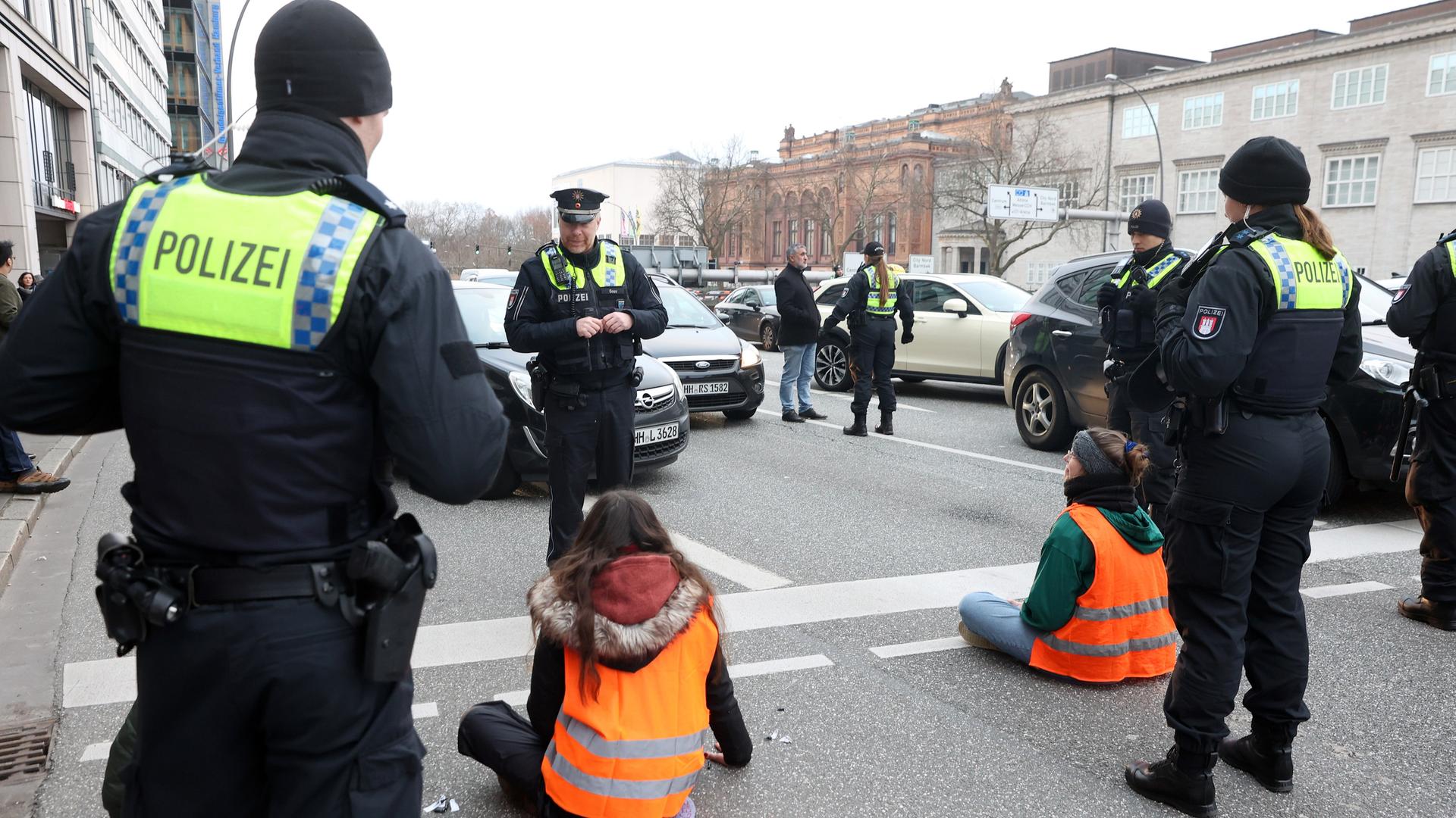 Klimaaktivisten blockieren eine Straße in Hamburg. Sie sind umringt von Polizisten, vor ihnen stauen sich Autos. (Symbolbild)