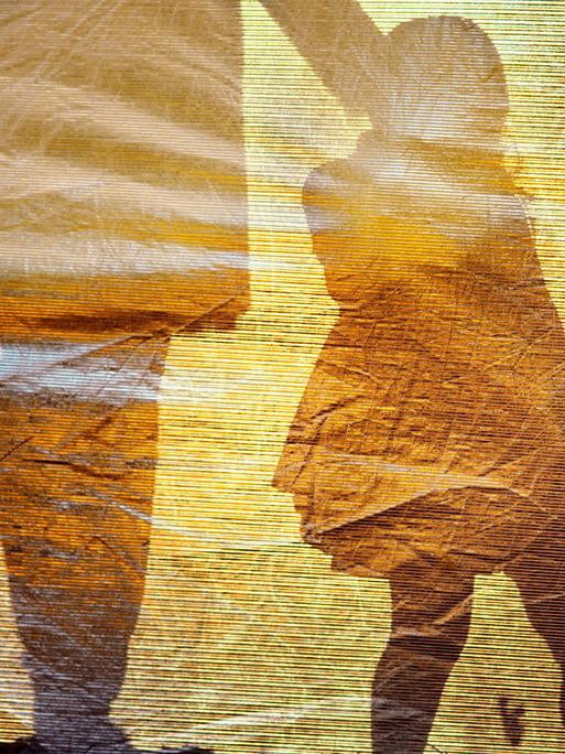 Der Schatten eines kleinen Mädchens an der Hand einer erwachsenen Person bildet sich auf einer goldfarbenen Oberfläche ab.