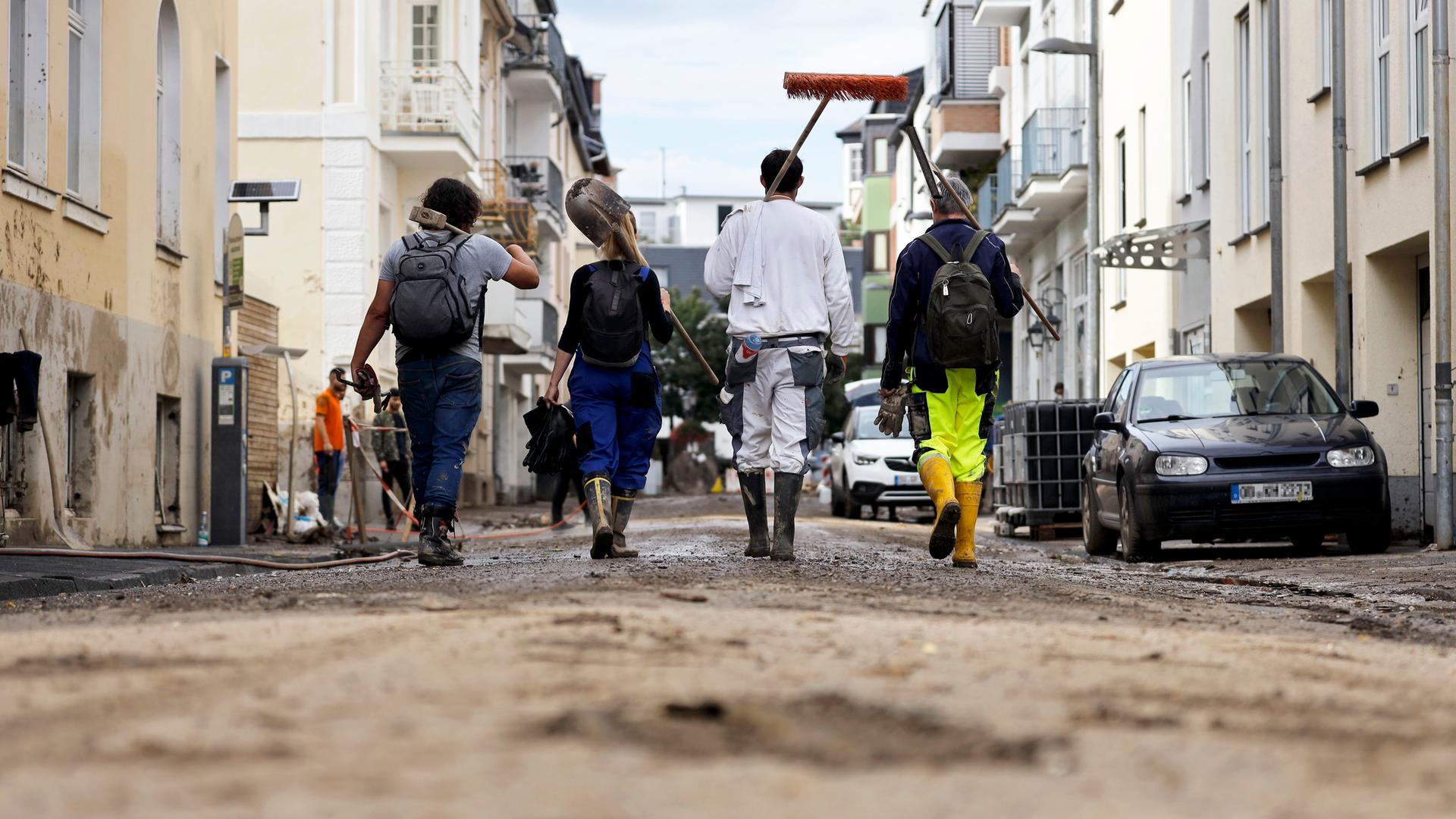 Rückansicht von Hilfskräften, die durch eine Straße gehen, auf der mit Schlamm und Schmutz noch die Folgen einer Flut zu erkennen sind