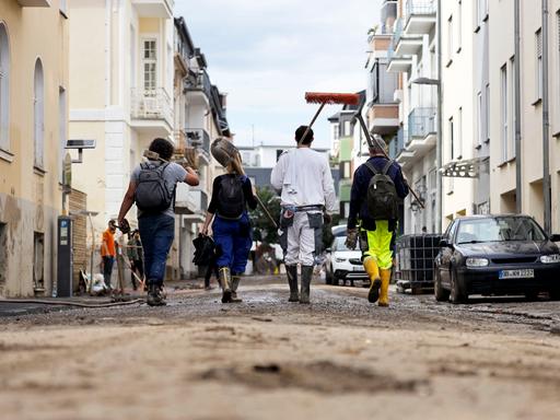 Rückansicht von Hilfskräften, die durch eine Straße gehen, auf der mit Schlamm und Schmutz noch die Folgen einer Flut zu erkennen sind