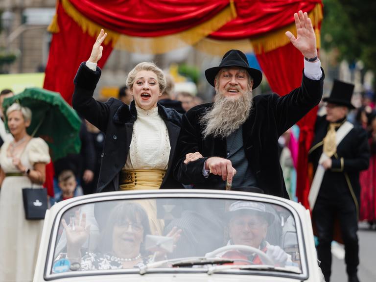 Als Theaterherzog und Helene Freifrau von Heldburg gekleidete Teilnehmer winken beim Festumzug zum 200. Geburtstag von Georg II. von Sachsen-Meiningen aus einem Oldtimer.