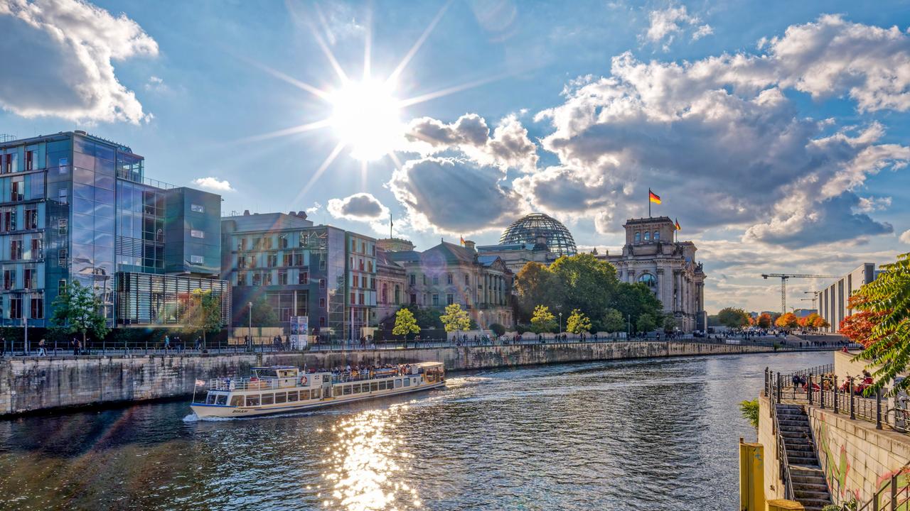 Spreeufer in Herbst mit dem Berliner Reichstag im Hintergrund, die Sonne scheint.