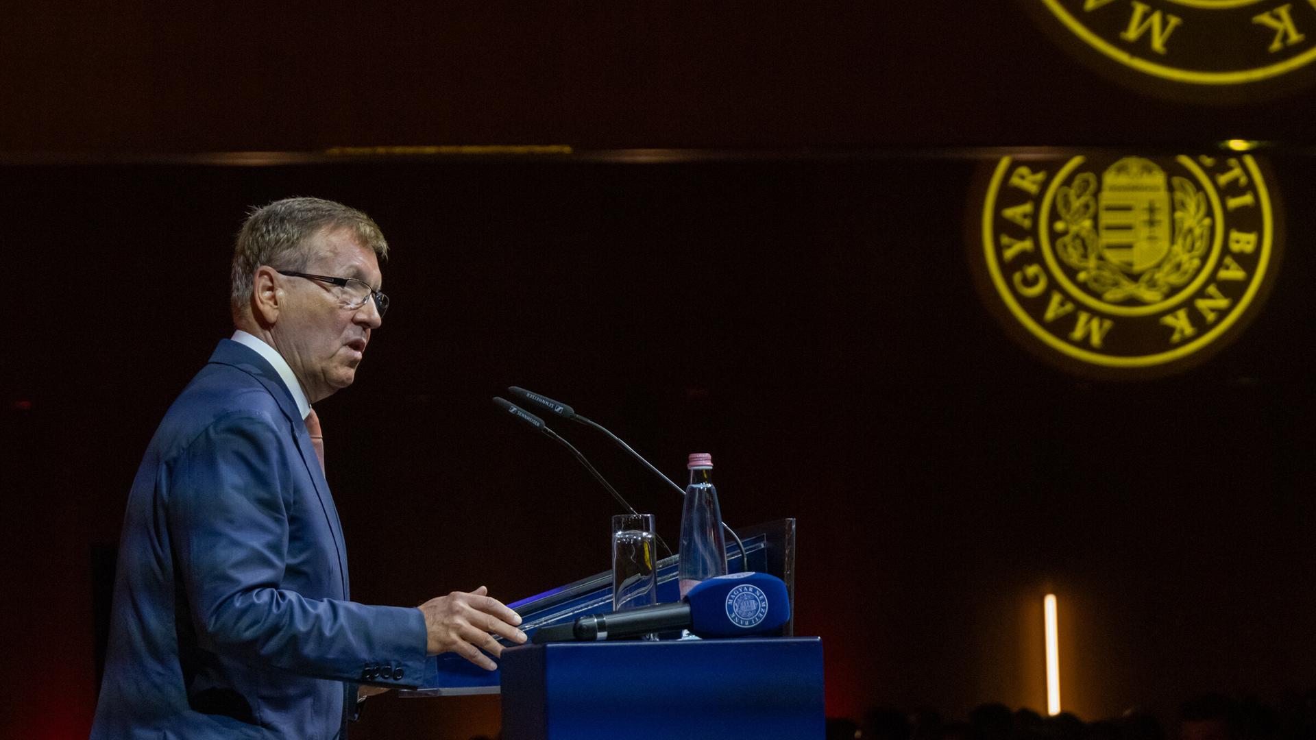 Matolcsy steht hinter einem Rednerpult. Er ist von der Seite fotografiert. Matolcsy steht hinter einem Rednerpult. Er ist von der Seite fotografiert.