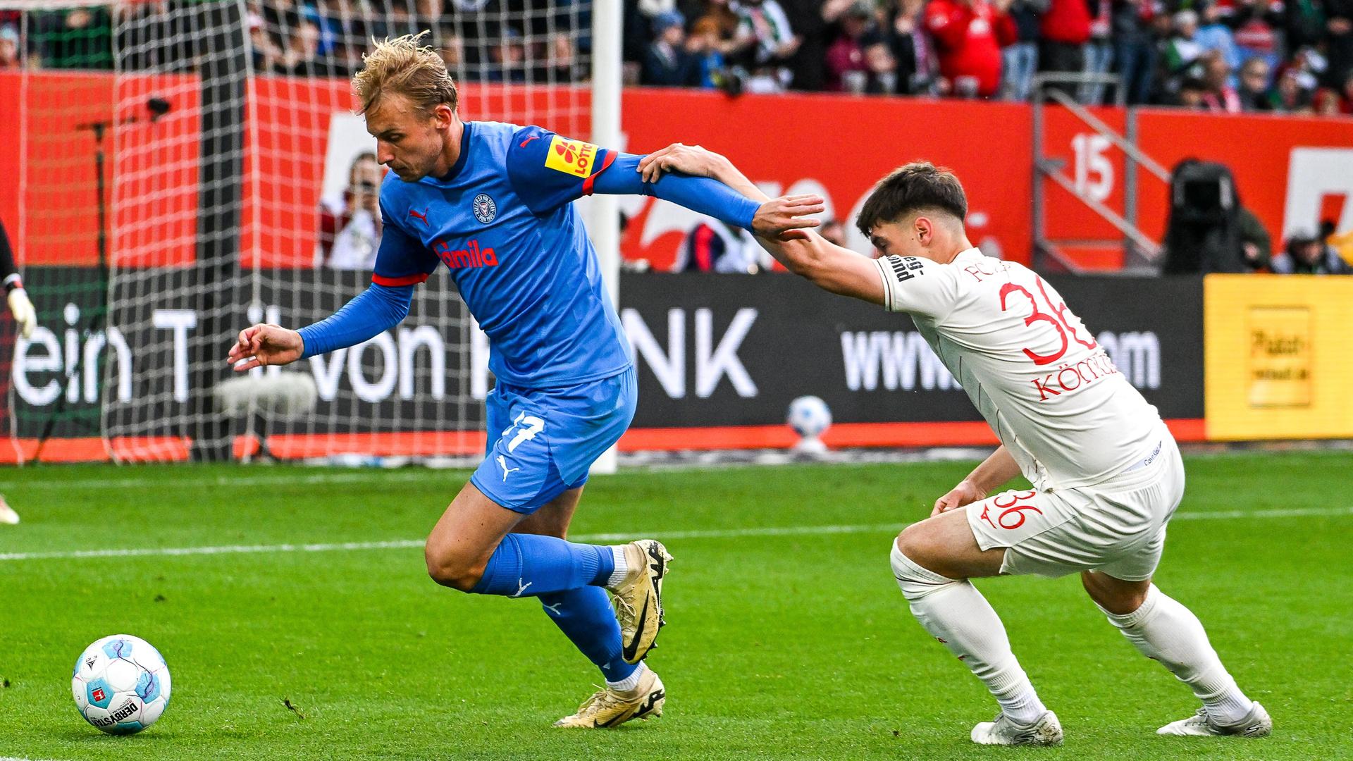 Timo Becker von Holstein Kiel im Zweikampf gegen Mert Kömür vom FC Augsburg