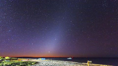 Nachthimmel mit Zodiakallicht am Meer in Westaustralien. Vor dem dunklen Himmel ist eine Art Lichterscheinung zu sehen, die wie ein Licht Richtung Strand zu scheinen scheint. 
