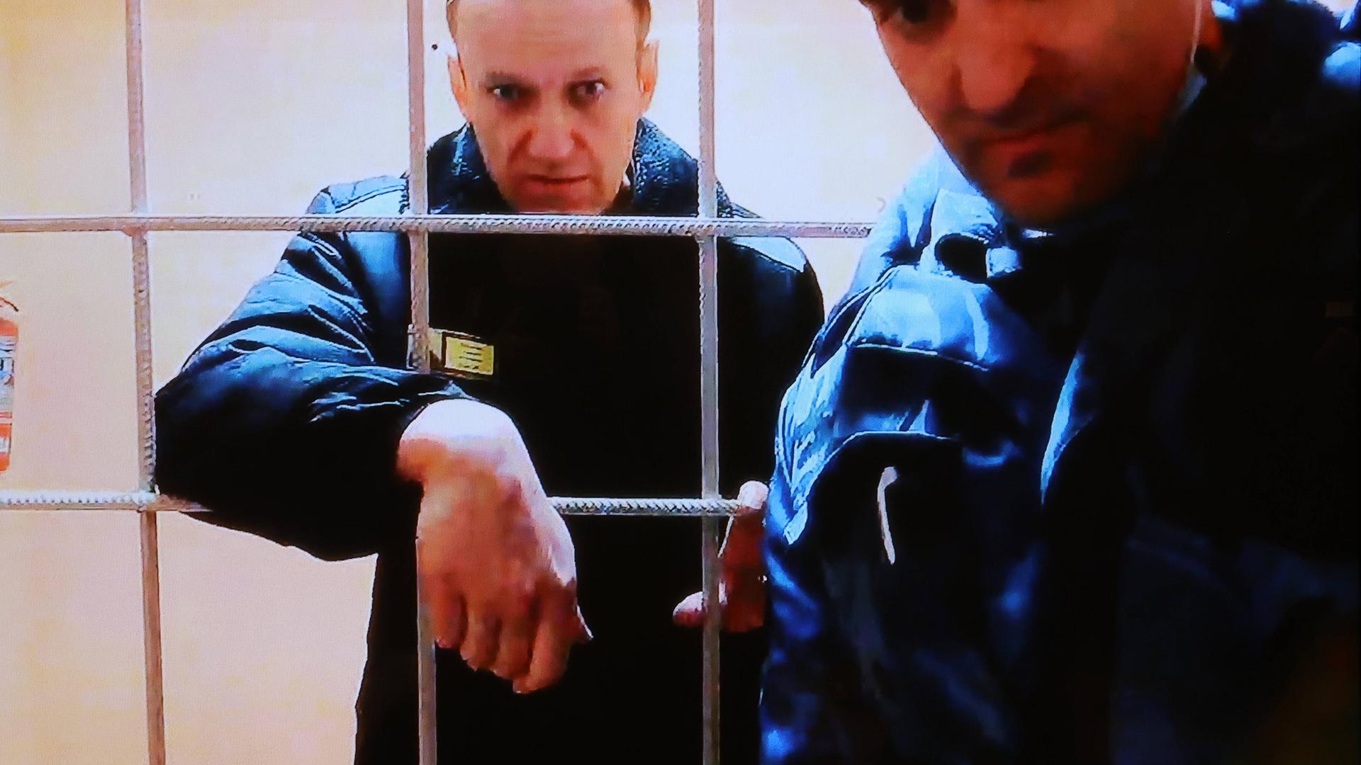Alexei Navalny hinter Gitterstäben, vor ihm steht ein Mann.