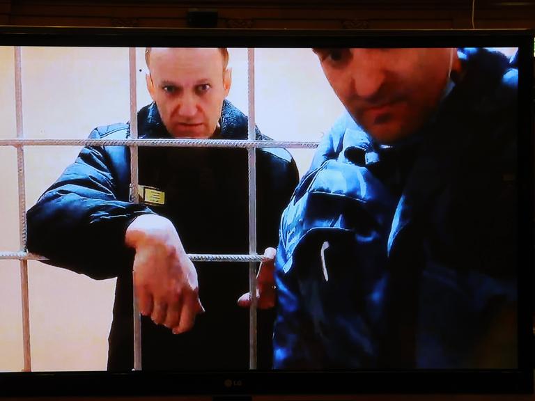 Alexei Navalny hinter Gitterstäben, vor ihm steht ein Mann.