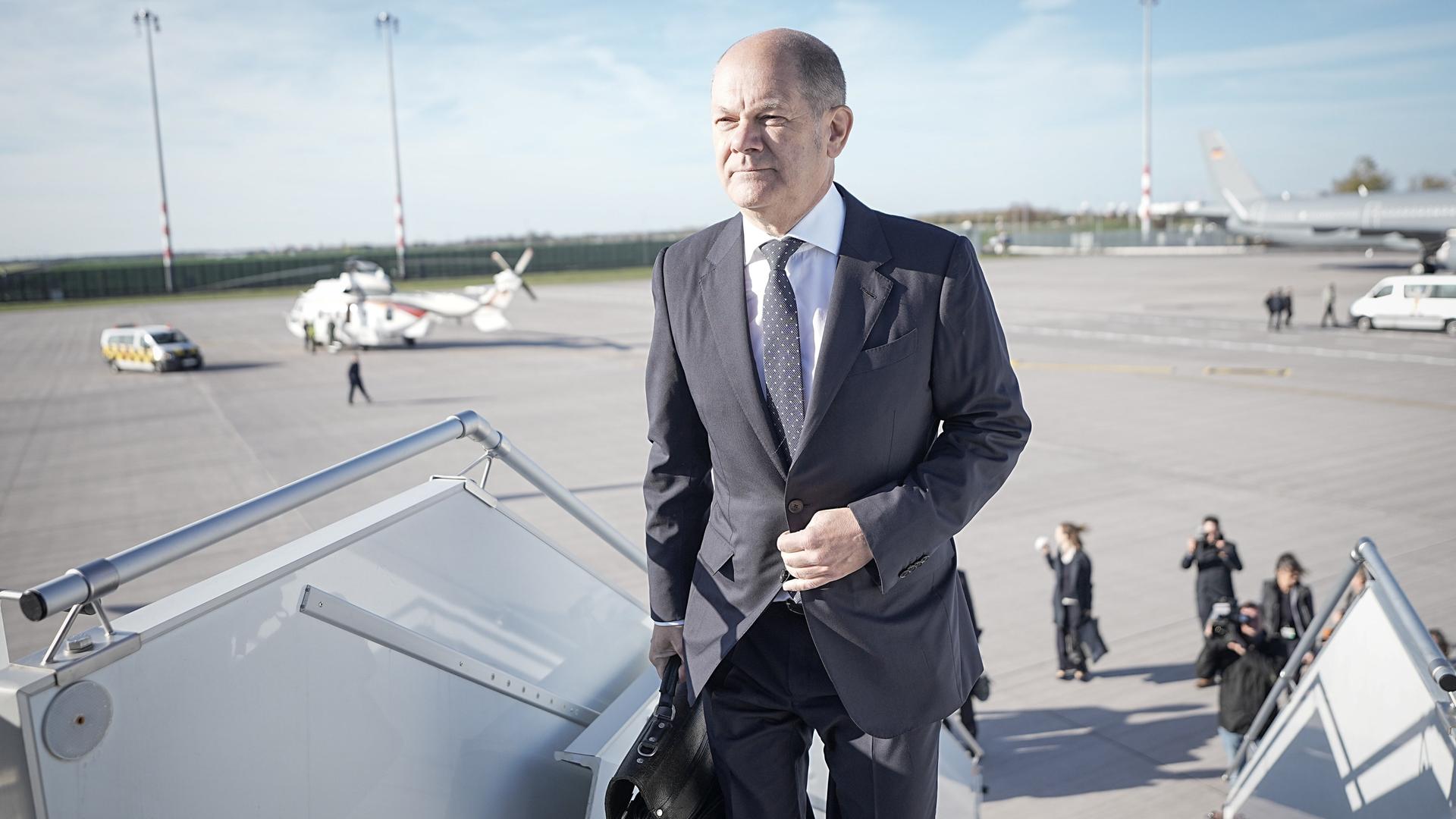 Kanzler Scholz betritt mit einer Aktentasche in der Hand über eine Treppe das Flugzeug.