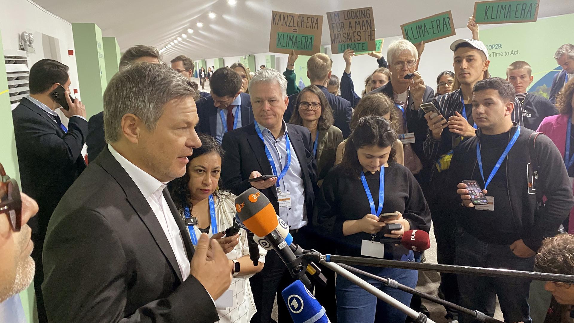 Baku: Robert Habeck (Bündnis 90/Die Grünen), Bundesminister für Wirtschaft und Klimaschutz, spricht auf der Weltklimakonferenz. Im Hintergrund stehen Aktivisten mit Plakaten.