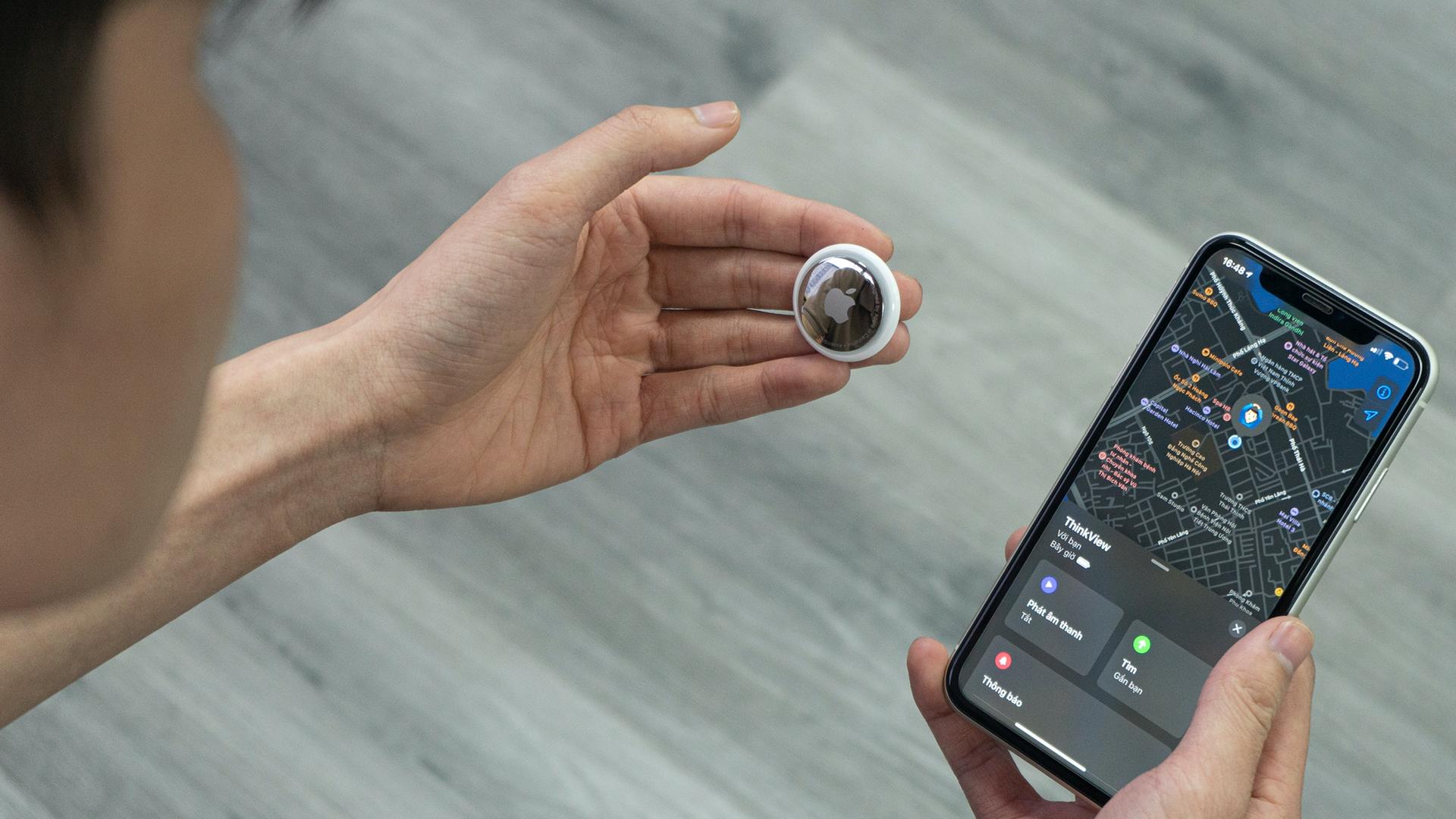 Eine Hand hält einen kleinen Bluetooth-Tracker, in diesem Fall ein AirTag von Apple, neben ein Smartphone.