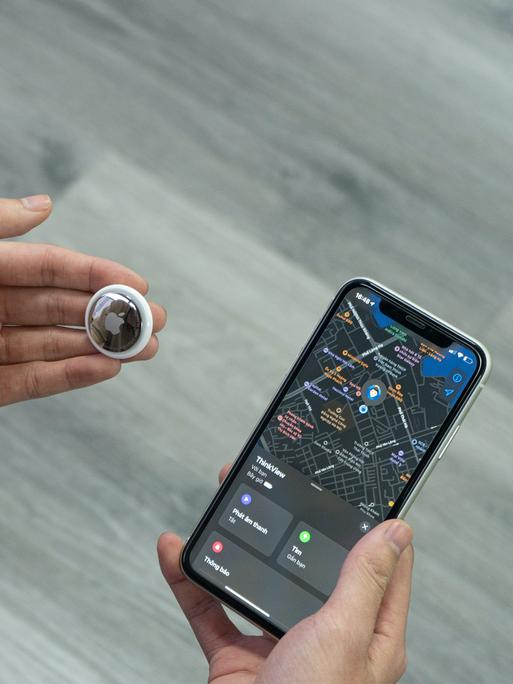 Eine Hand hält einen kleinen Bluetooth-Tracker, in diesem Fall ein AirTag von Apple, neben ein Smartphone.