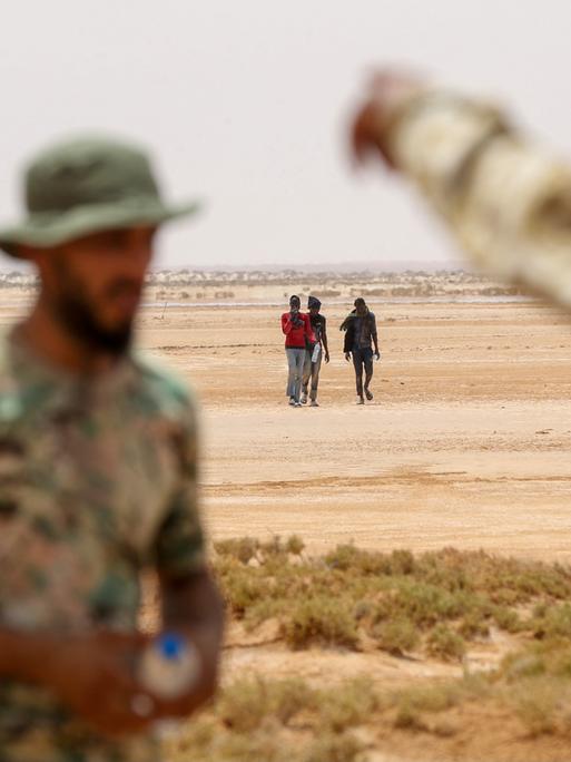 Libysche Grenzposten beobachten eine kleine Gruppe Flüchtender, die nah der libysch-tunesischen Grenze durch unbewohntes Gebiet laufen.