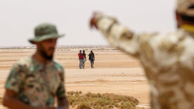 Libysche Grenzposten beobachten eine kleine Gruppe Flüchtender, die nah der libysch-tunesischen Grenze durch unbewohntes Gebiet laufen.