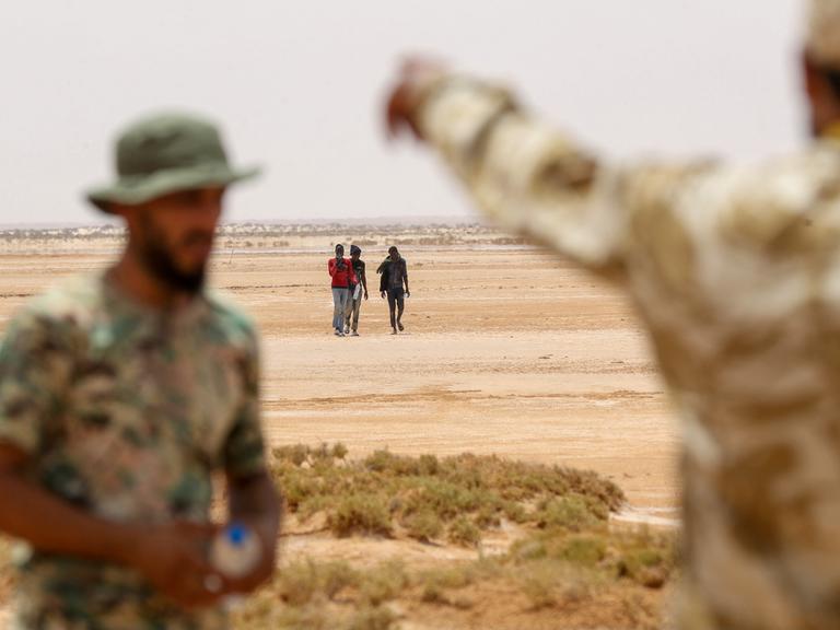 Libysche Grenzposten beobachten eine kleine Gruppe Flüchtender, die nah der libysch-tunesischen Grenze durch unbewohntes Gebiet laufen.