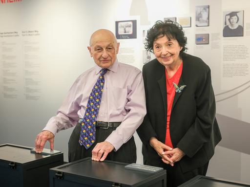 Kurt S. Maier und Inge Auerbacher stehen vor einer Ausstellungswand im Museum und lachen in die Kamera. Er trägt eine farbenfrohe Krawatte, sie eine Schmetterlingsbrosche an der Jacke. Kurt S. Maier und Inge Auerbacher stehen vor einer Ausstellungswand im Museum und lachen in die Kamera. Er trägt eine farbenfrohe Krawatte, sie eine Schmetterlingsbrosche an der Jacke.