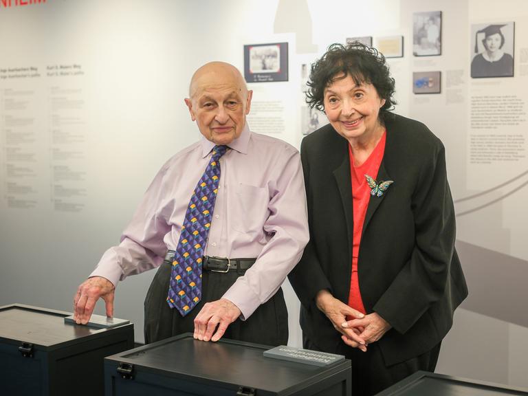 Kurt S. Maier und Inge Auerbacher stehen vor einer Ausstellungswand im Museum und lachen in die Kamera. Er trägt eine farbenfrohe Krawatte, sie eine Schmetterlingsbrosche an der Jacke. 