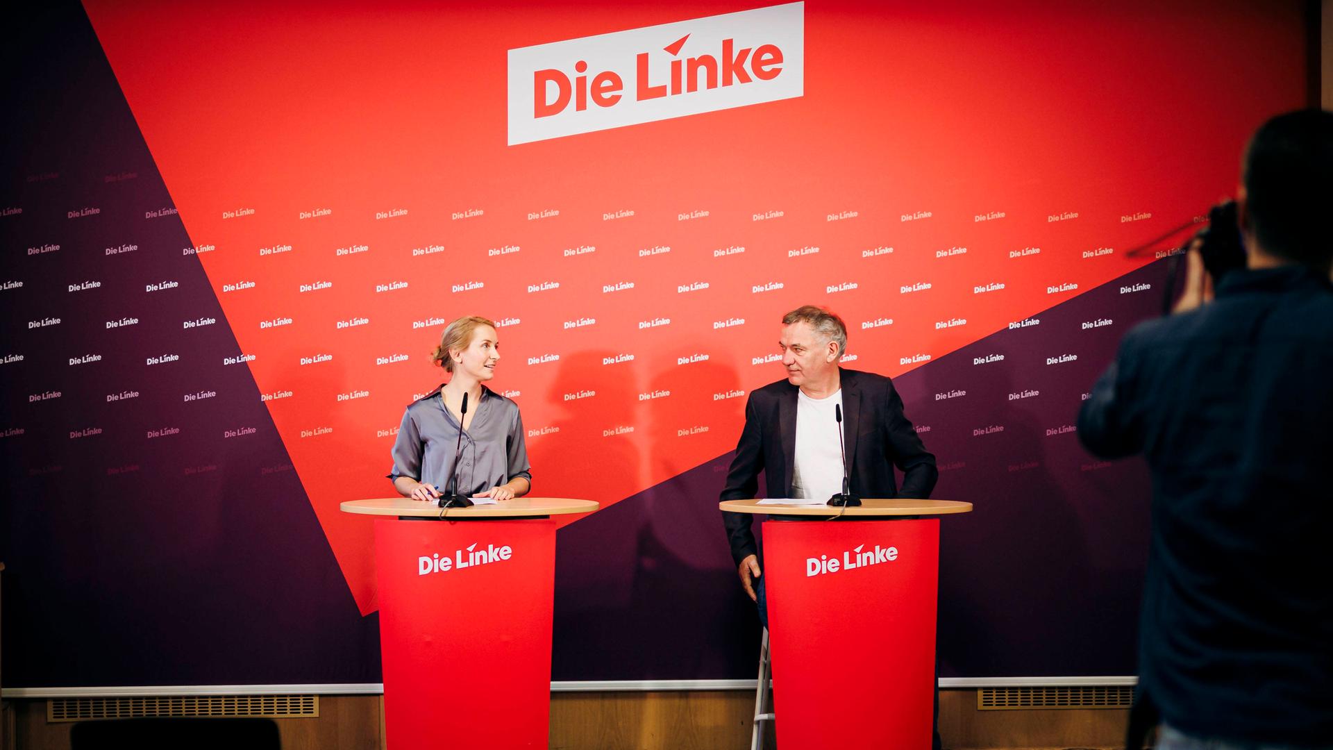 Jan van Aken und Ines Schwerdtner, Vorsitzenden der Partei Die Linke, blicken sich bei einer Pressekonferenz an. Im Hintergrund sieht man den Schriftzug "Die Linke".