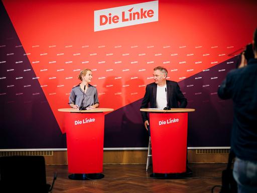 Jan van Aken und Ines Schwerdtner, Vorsitzenden der Partei Die Linke, blicken sich bei einer Pressekonferenz an. Im Hintergrund sieht man den Schriftzug "Die Linke".