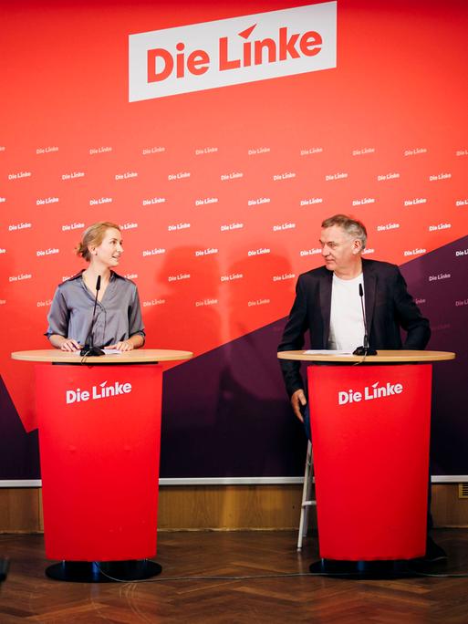 Jan van Aken und Ines Schwerdtner, Vorsitzenden der Partei Die Linke, blicken sich bei einer Pressekonferenz an. Im Hintergrund sieht man den Schriftzug "Die Linke".