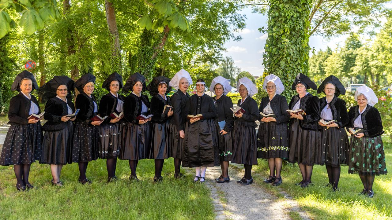 Frauen in traditioneller Tracht aus schwarzer Jacke, dunklen, teils grün besticktem Rock, und weißer oder schwarzer Haube stehen nebeneinander.