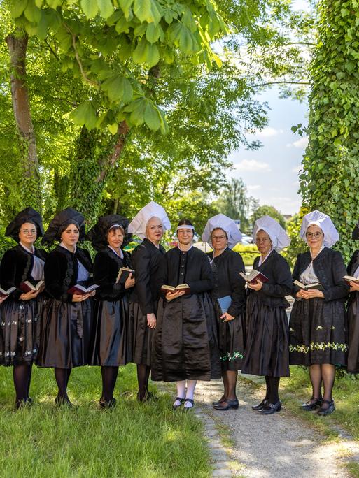 Frauen in traditioneller Tracht aus schwarzer Jacke, dunklen, teils grün besticktem Rock, und weißer oder schwarzer Haube stehen nebeneinander.