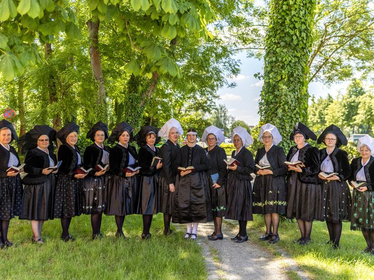 Frauen in traditioneller Tracht aus schwarzer Jacke, dunklen, teils grün besticktem Rock, und weißer oder schwarzer Haube stehen nebeneinander.