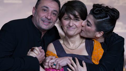 Sepideh Farsi steht zwischen einem Mann und einer Frau, die sie umarmen. Sie selbst lächelt in die Kamera.