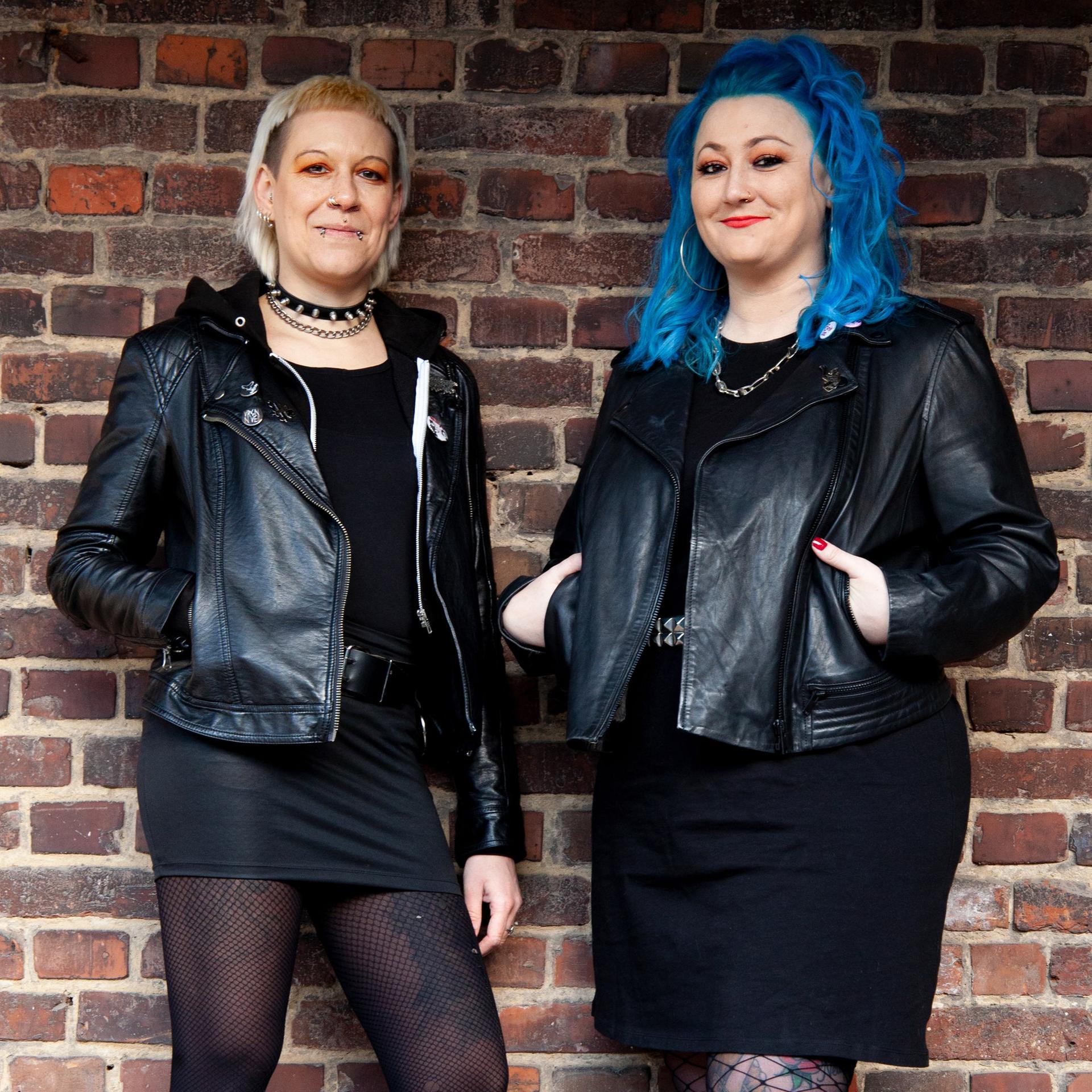Diana Ringelsiep und Ronja Schwikowski stehen in punk-typischer Aufmachung vor einer Backsteinmauer und schauen in die Kamera.