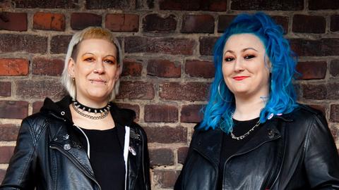 Diana Ringelsiep und Ronja Schwikowski stehen in punk-typischer Aufmachung vor einer Backsteinmauer und schauen in die Kamera.