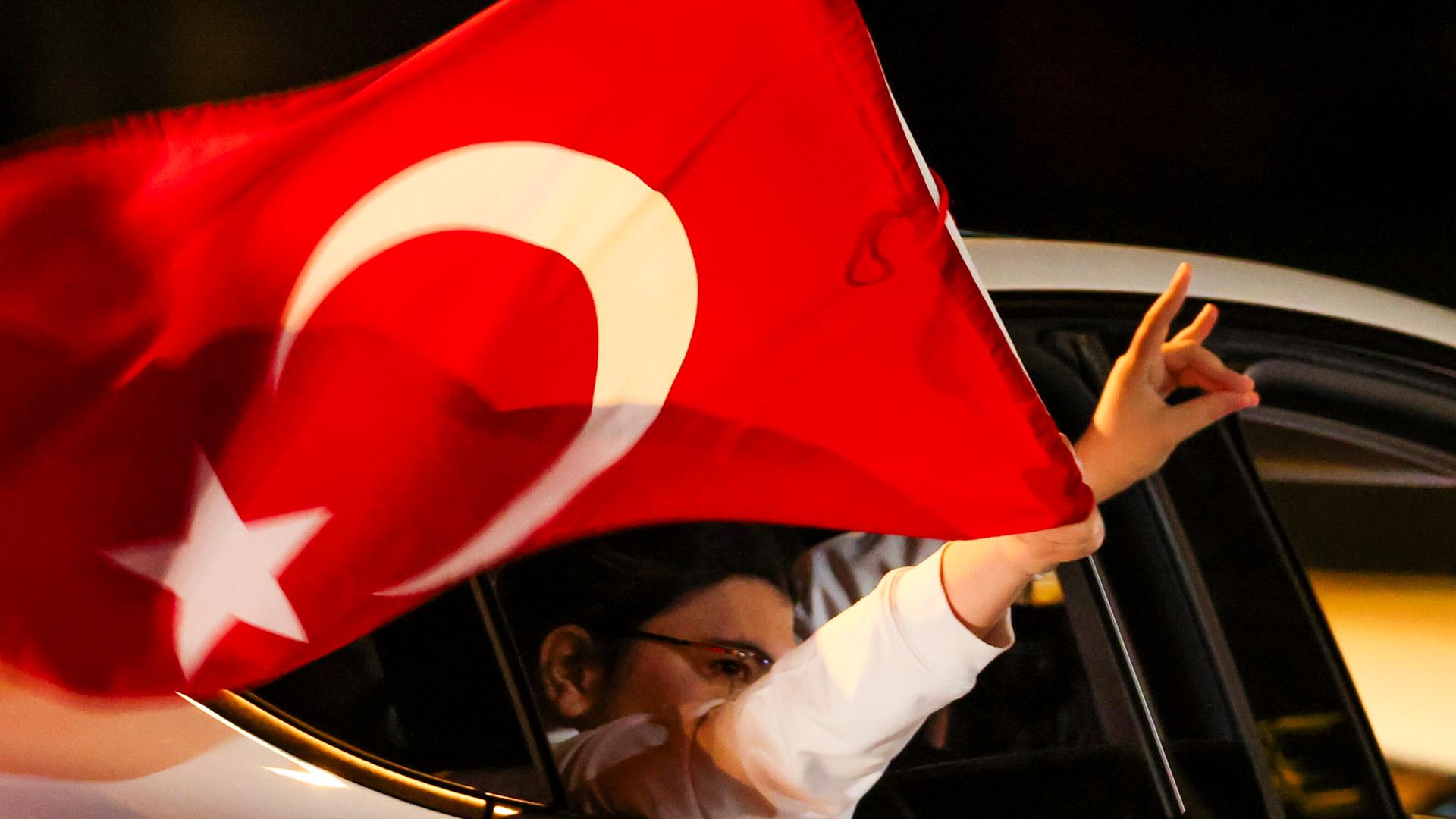 Aus einem Auto mit türkischer Fahne ragt eine Hand, die den sogenannten Wolfsgruß macht.