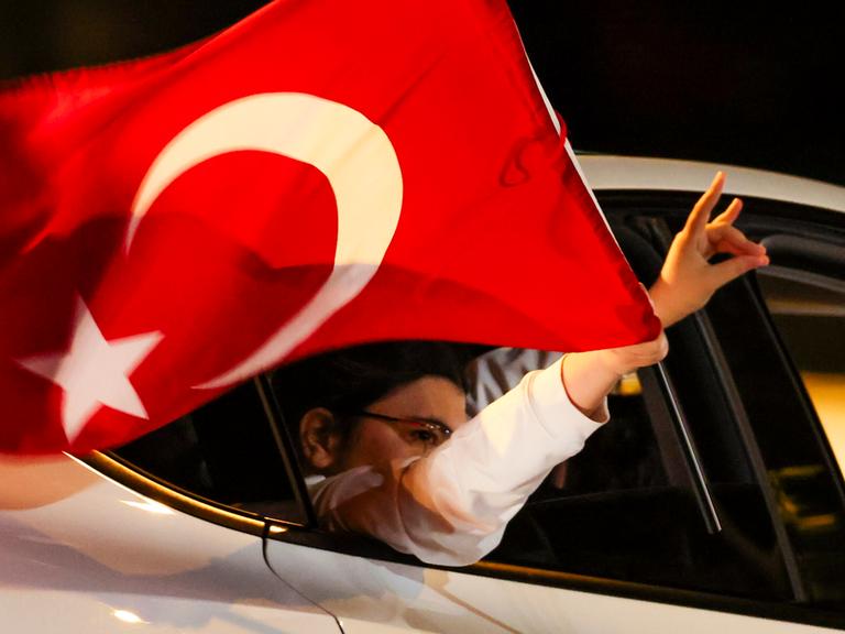 Aus einem Auto mit türkischer Fahne ragt eine Hand, die den sogenannten Wolfsgruß macht.