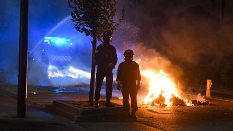 Zwei Feuerwehrleute stehen mit ihrem Einsatzwagen vor einem Brand.