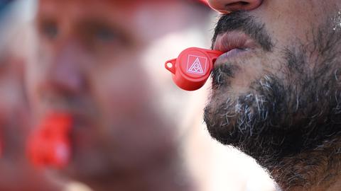 Zwei Männer halten IG-Metall-Pfeifen zwischen den Lippen. 