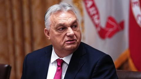 Victor Orbán blickt vor Flaggen ernst zur Seite