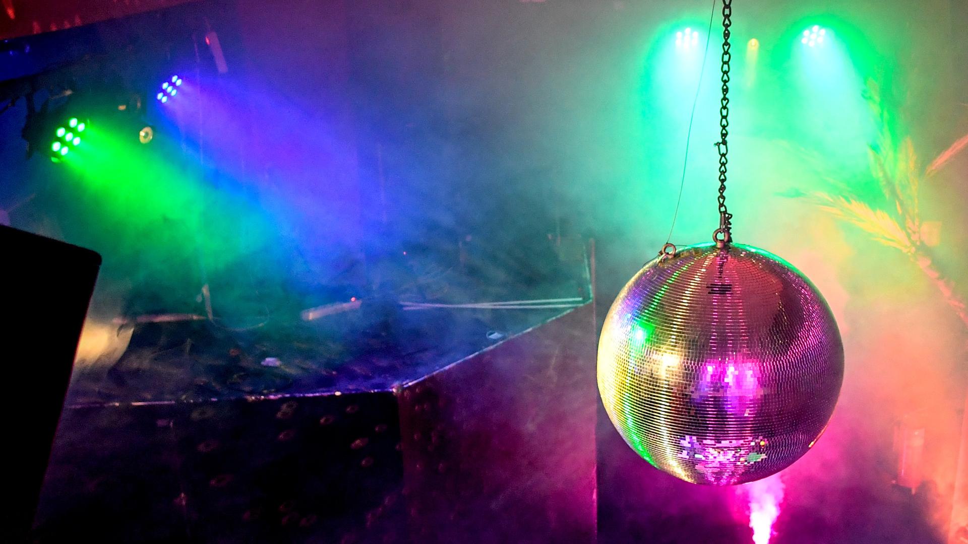 Eine Diskokugel dreht sich in einem Club und reflektiert das einfallende Licht der Scheinwerfer und Lampen.