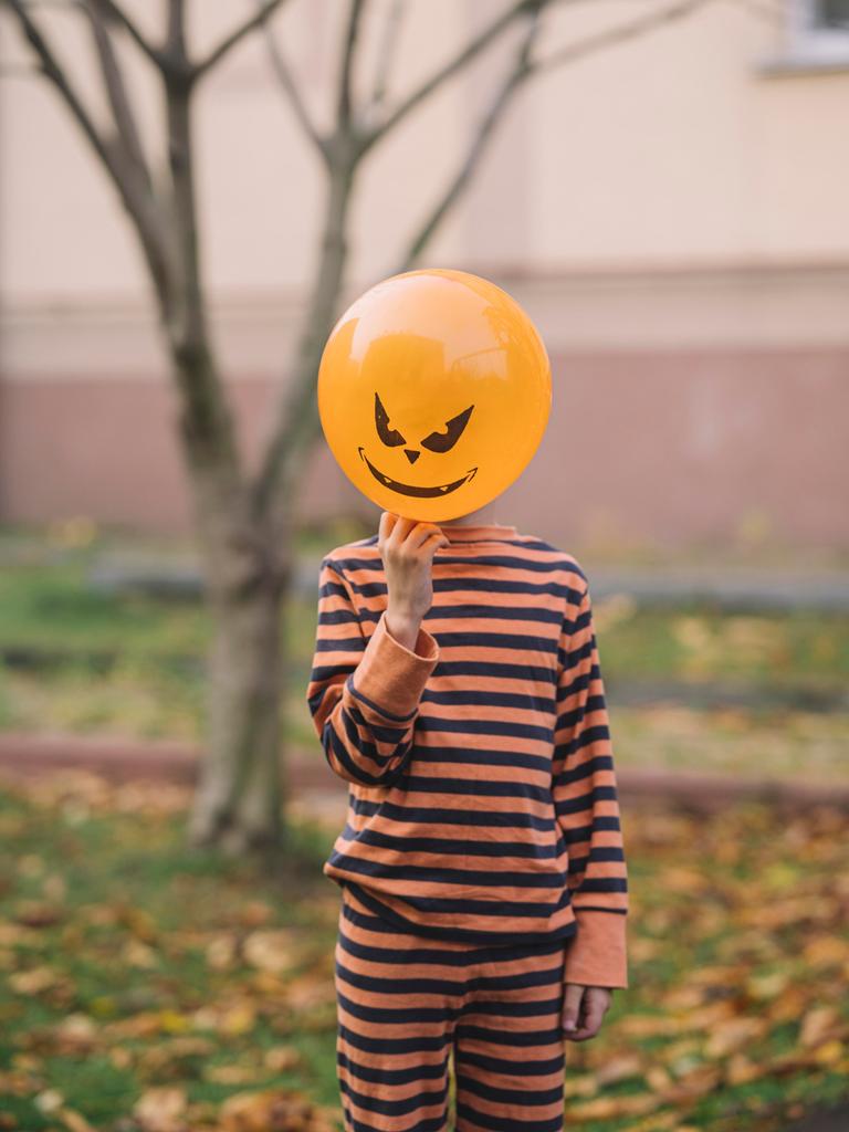 Ein Kind hält einen orangenen Luftballon mit Teufelsfratze vor sein Gesicht